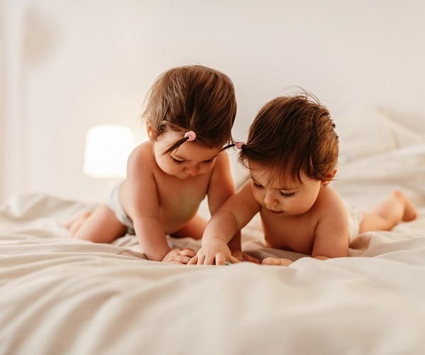 Two baby girls lying on the bed , looking at a mobile phone